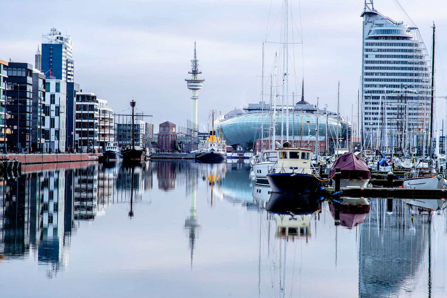 photo-1618588977486-25bcd81f2b5e Fotografie des Hafenbeckens Neuer Hafen in Bremerhaven. Blick auf das Klimahaus Bremerhaven und das Hotel ATLANTIC Sail City. Im Vordergrund Segelboote.
